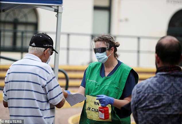 A healthcare professional holding a bottle of handsanitiser talks to people at a pop-up clinic testing for the coronavirus disease at Bondi Beach on Wednesday (pictured)