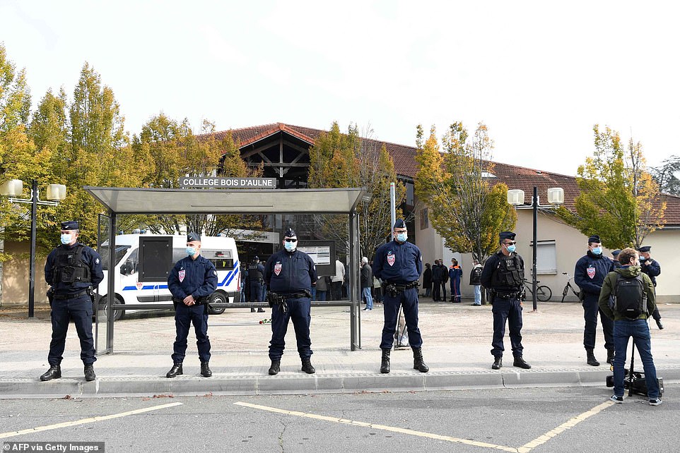 French police officers stand as adults and children gather in front of flowers displayed at the entrance of the school in Paris