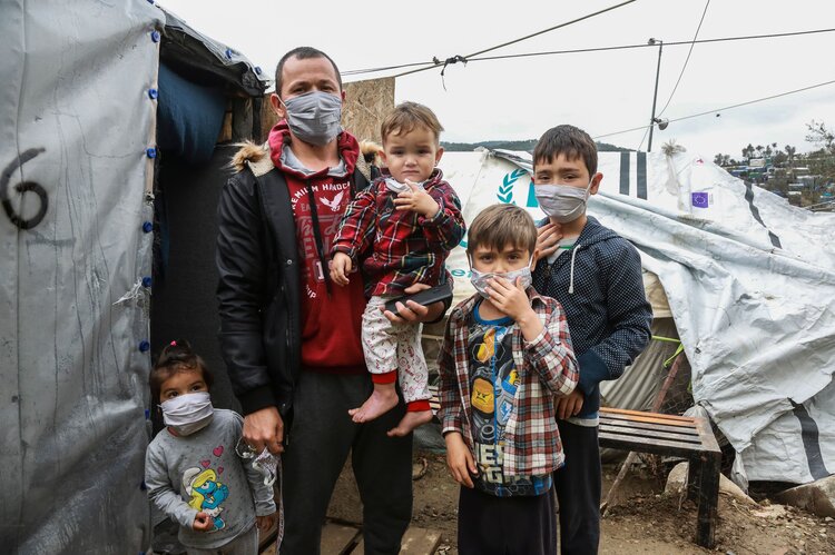 A migrant family wearing handmade protective face masks stand next to their tent in the camp of Moria in the island of Lesbos on March 28, 2020 as as the country is under lockdown to stop the spread of Covid-19 disease caused by the novel coronavirus. (Photo by Manolis LAGOUTARIS / AFP) (Photo by MANOLIS LAGOUTARIS/AFP via Getty Images)