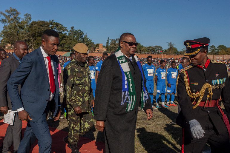 Malawi President Arthur Peter Mutharika C wears two football club scarves of the teams of a friendly match as part of national celebrations to commemorate the countrys 54th Independence Anniversary July 6 2018 Photo by Amos Gumulira  AFP