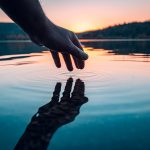 Finger touches surface of mountain lake Hand reflection