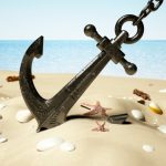 Black anchor with chain stuck on the sand by the seashore