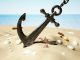 Black anchor with chain stuck on the sand by the seashore.